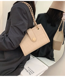Detail of beige crocodile pattern handbag with elegant gold chain and woven strap