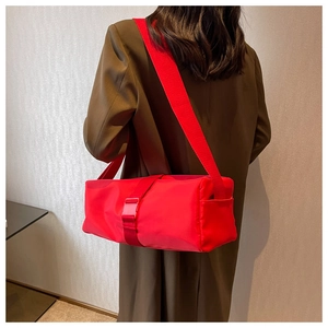 Detail of red nylon cylinder crossbody bag featuring a wide strap and plastic buckle closure
