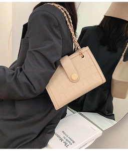 Detail of beige crocodile pattern bag with chain strap and round wooden metal clasp