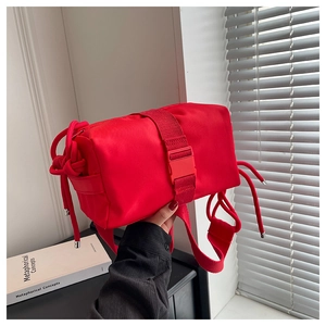 Detail of red nylon crossbody bag featuring wide strap with plastic buckle and drawstrings