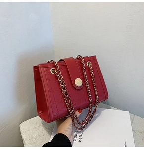 Detail of red crocodile pattern bridal bag with dual gold chain straps on a stone surface