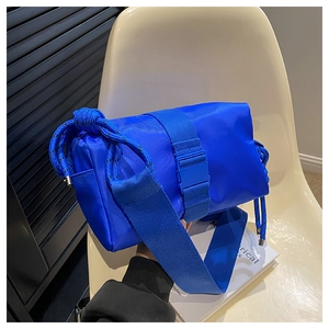 Detail of royal blue nylon crossbody bag with wide strap and plastic buckle on white chair