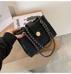 Detail of black crocodile texture bag with gold chain strap and metallic buckle