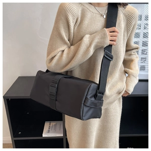 Detail of a black nylon cylinder crossbody bag featuring a secure buckle and wide strap