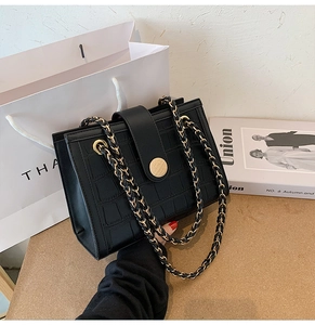 Detail of black crocodile embossed shoulder bag with gold clasp and chain strap