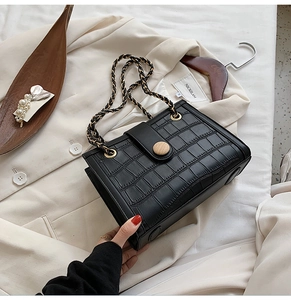 Macro shot of black crocodile embossed square bag with gold chain and wooden button