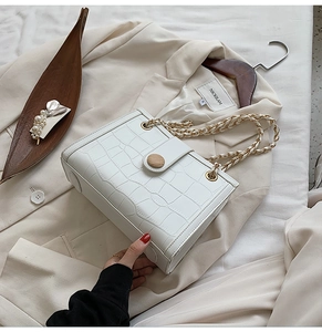 Close-up of white crocodile pattern handbag with wooden buckle and golden chain strap