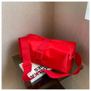 Detail view of bright red nylon cylindrical crossbody bag with wide fabric strap