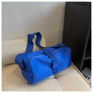 Close-up of a blue nylon cylinder shoulder bag with buckle detail on a quilted cushion