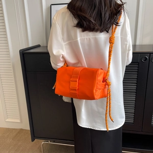 Bright orange nylon crossbody bag with bold woven rope strap shown on a model
