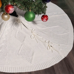 Falda blanca tejida para árbol de Navidad con trenzado y lazos sobre suelo oscuro
