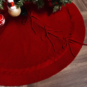 Close-up of red cable knit Christmas tree skirt with bow tie closures on wooden floor