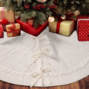 Detailed cable knit white Christmas tree skirt with ribbon bows on wooden floor