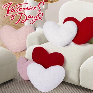 Close-up of heart-shaped teddy fleece pillows in pink, red, and white on a cozy sofa