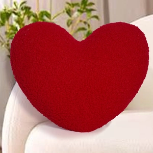 Detailed view of red heart-shaped pillow with textured bouclé fabric on a leather sofa