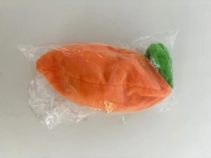 Detail of creative plush carrot toy with green leaves and orange fabric in clear packaging