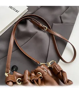 Detail of adjustable leather strap and golden buckle on a brown drawstring bucket bag