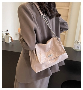 Close-up of beige pleated tote bag with metal chain strap worn by a model in a cafe