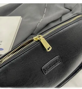Gros plan du zip doré et logo embossé sur le sac en cuir noir à grain de litchi