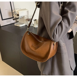 Détail du sac demi-lune en cuir marron avec fermeture éclair dorée et logo embossé