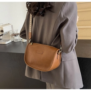 Détail d'un sac demi-lune en cuir marron avec sangle tissée et ferrures dorées