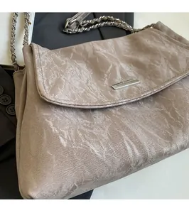 Detail showing wrinkled texture fabric, metal chain strap and logo plate on beige tote bag
