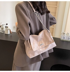 Elegant pleated beige tote bag with silver chain strap shown in a modern cafe setting