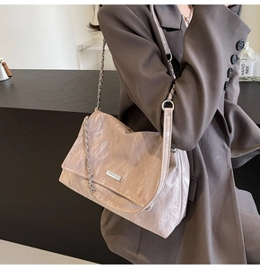 Detail of pink pleated tote bag with metal chain strap and logo plate on a shoulder