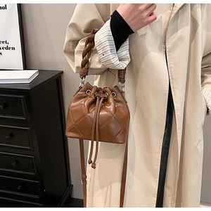 Detail of brown quilted bucket bag with woven handle and drawstring closure on model