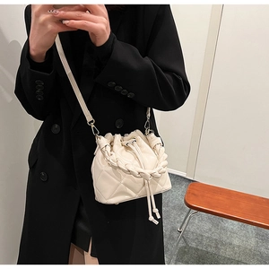 Quilted cream bucket bag with woven handle and drawstring shown in a mirror selfie