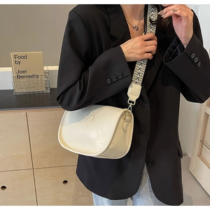 Sac bandoulière beige avec large sangle ethnique et logo métallique en gros plan