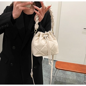 Detail of cream quilted bucket bag with woven handle and drawstring closure shown in use
