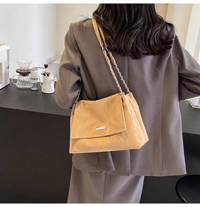 Detail of a beige pleated shoulder bag with chain strap worn with a brown blazer