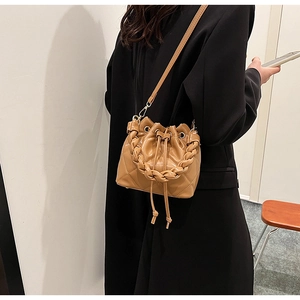 Detail of caramel bucket bag with diamond quilting and woven handle on a black blazer