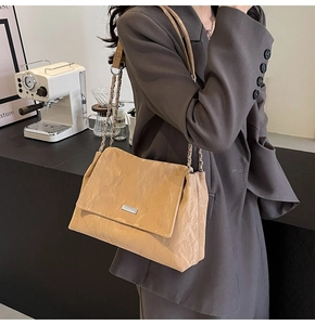 Detail of khaki pleated tote bag with chain strap styled with a grey blazer at a cafe