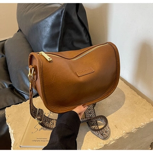 Détail d'un sac selle demi-lune marron avec une large bandoulière tissée ethnique