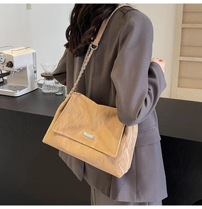 Detail of khaki pleated tote bag featuring a silver chain strap and metal logo plaque