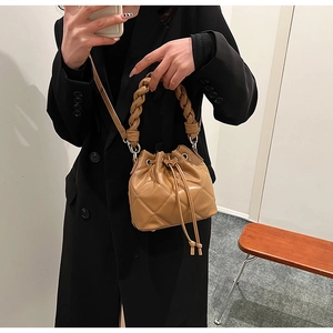 Detail of tan quilted bucket bag featuring a braided handle and adjustable shoulder strap