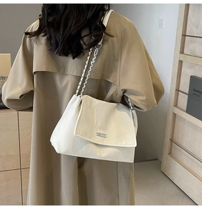 Detail of a beige quilted tote bag with silver chain strap worn with a khaki trench coat