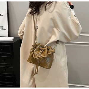 Brown quilted bucket bag with woven handle and drawstring closure worn with a beige coat