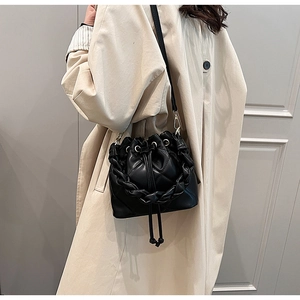 Close-up of black quilted leather bucket bag with thick woven chain handle on a trench coat