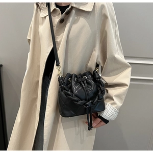 Detail of black quilted bucket bag with twisted handle on beige trench coat