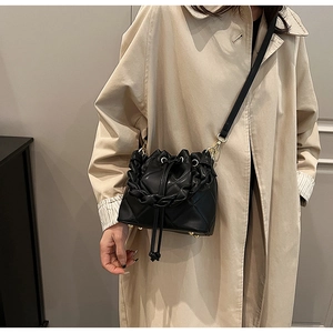 Detail of black quilted bucket bag with ruffle handle and adjustable shoulder strap