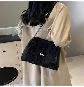 Detail of black pleated tote bag showing metallic chain strap and silver logo plaque