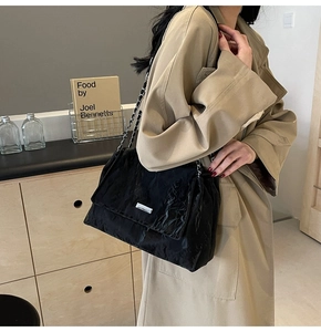 Detail of black pleated tote bag with silver chain strap and metal logo on a stylish model