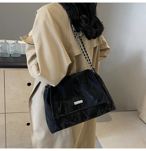 Detail of black pleated tote bag featuring a chain shoulder strap and metal logo plaque