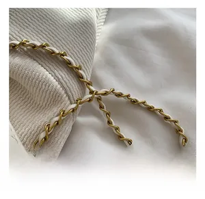 Macro detail of golden metal chain woven with white leather on a quilted bucket bag