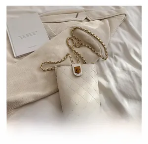 Detail of white quilted bucket bag with gold chain strap on soft textured bedding