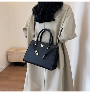 Detailed view of black pebbled leather tote bag with gold hardware worn with a beige coat