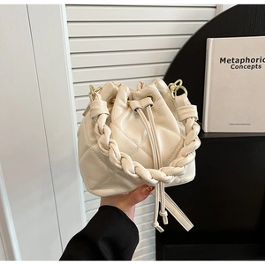 Detail of cream quilted bucket bag with braided handle and gold drawstring eyelets